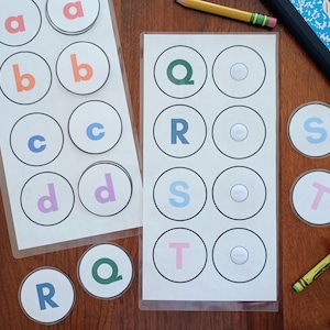 May include: Two laminated sheets featuring rows of circular cutouts with lowercase and uppercase letters in various colors including red, orange, blue, purple, green, and pink. Several loose circular letter tokens are placed nearby.