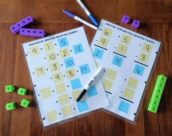 Puede incluir: Dos hojas de trabajo plastificadas tituladas Horizontal Addition Equation Frames y Vertical Subtraction Equation Frames con cuadrados amarillos y azules para números, acompañadas de cubos de conteo de plástico y marcadores borrables.