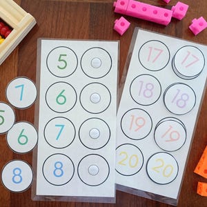 May include: Educational math learning set featuring two laminated sheets with circular number cards from 5 to 20, a wooden abacus with colorful beads, and several pink and orange plastic interlocking cubes for counting and number recognition practice.