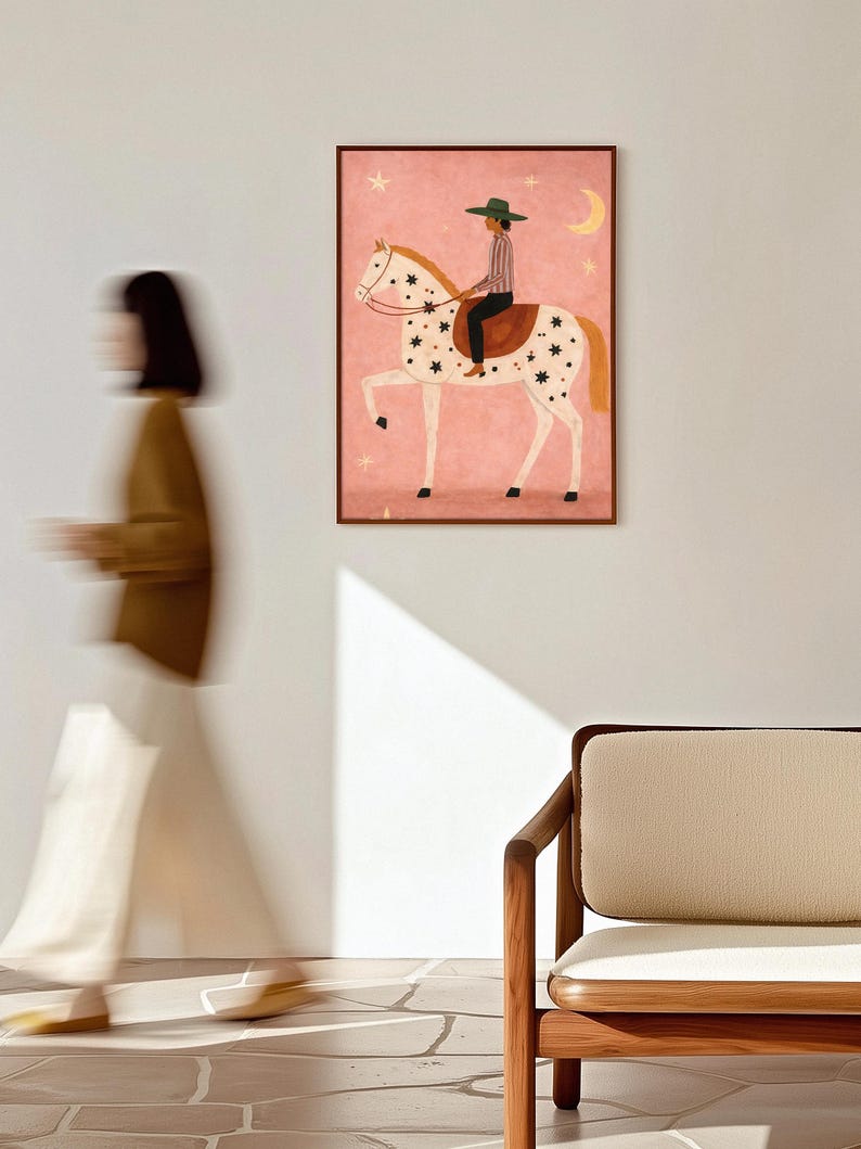 May include: A framed art print depicts a person riding a white horse adorned with black star-shaped spots. The rider wears a green hat and striped shirt. The background is pink with stars and a crescent moon.