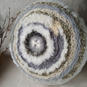 Può includere: Gomitolo di lana rotondo e strutturato con anelli concentrici di filato grigio, bianco, beige e verde. Il centro presenta un tessuto intrecciato. Ideale per progetti di maglia o uncinetto.