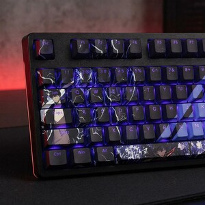 Könnte beinhalten: Schwarze mechanische Tastatur mit individuellen Tastenkappen. Die Tastenkappen haben ein Marmordesign mit violetter Hintergrundbeleuchtung. Einige Tastenkappen haben Anime-Charakter-Illustrationen. Die Tastatur hat einen schwarzen Rahmen mit rotem Akzent an der Seite.
