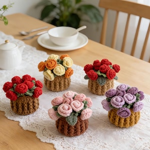 Könnte beinhalten: Fünf handgefertigte Häkelblumenarrangements in kleinen braunen Körben. Die Blumen sind in Rot-, Orange-, Gelb-, Rosa- und Lilatönen gehalten. Die Körbe stehen auf einer weißen Spitzentischdecke auf einem Holztisch.