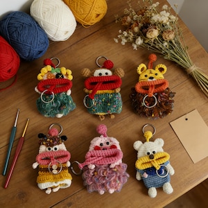 May include: Six handmade crochet keyrings in animal designs, including a tiger, bear, and cow. Each keyring features a unique colour palette and intricate details, with key rings attached for easy use. The keyrings are displayed on a wooden surface.