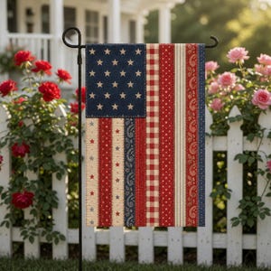 May include: A decorative garden flag featuring a patchwork design of the American flag. The flag has a blue field with white stars, red and white stripes, and paisley and gingham patterns. The flag is displayed on a black metal stand.