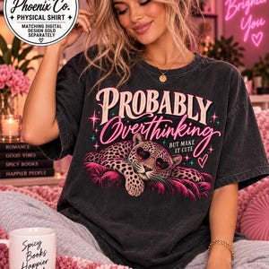 May include: A charcoal gray short-sleeve t-shirt featuring a graphic of a leopard wearing heart-shaped sunglasses, resting on a pink cushion. The text reads "Probably Overthinking" in pink and cream, with "BUT MAKE IT CUTE" in smaller white letters.