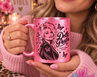 May include: A metallic pink ceramic mug featuring a black graphic illustration of Dolly Parton with long wavy hair, butterflies, and stars. The text reads Dolly Parton and country glam forever. The mug has a handle on the left side and a smooth finish.