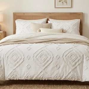 May include: A white, textured duvet cover with a geometric diamond design. The bed is made with matching pillows and a neutral-toned throw. A wooden headboard and bedside table complete the bedroom setting.