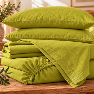 May include: A bedding set in a vibrant lime green color, featuring two rectangular pillowcases stacked on top of a folded flat sheet and a fitted sheet with elasticized edges, all made from a textured fabric with a visible weave.