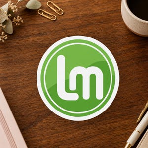 May include: A circular sticker featuring a vibrant green background with a white border and the white lowercase letters lm centered in the middle. The design has a glossy finish with a subtle diagonal light reflection across the green surface.