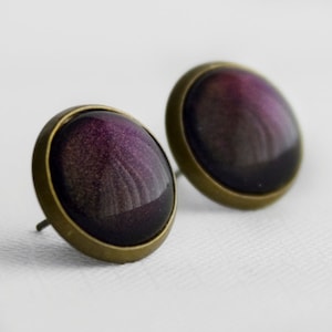 Puede incluir: Un par de pendientes de botón de bronce con un cabujón redondo, iridiscente morado y negro.