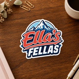 May include: A die-cut sticker featuring a graphic of snow-capped blue mountains above the text "Ella's FELLAS" in a bold, red and white athletic-style font with a dark blue outline, set against a light blue circular background element.