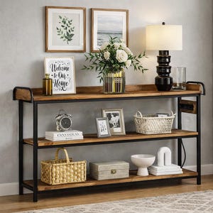 May include: A three-tiered, rustic-style console table with a black metal frame and wooden shelves. The top shelf displays a lamp, framed art, and a vase of flowers. Decorative items like a clock, baskets, and books are on the lower shelves. The framed sign reads "Welcome to Our Home."
