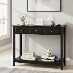May include: Black console table with three drawers and gold knobs. The table has a lower shelf with decorative boxes, books, and a small sculpture. A lamp, picture frame, and plant sit on top.