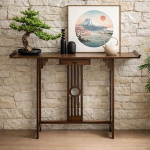 May include: A dark brown wooden console table with a drawer and decorative vertical slats. A bonsai tree, black vase, and a framed print of a mountain landscape are displayed on the table. The table has a built-in shelf on each side.