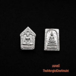 Può includere: Due amuleti in metallo color argento con figure di Buddha in rilievo in posizione seduta. Un amuleto ha una parte superiore appuntita con dettagli decorati, mentre l'altro è rettangolare con una cornice ad arco. Testo: มงคลดี ThaiMongkolDeeAmulet.