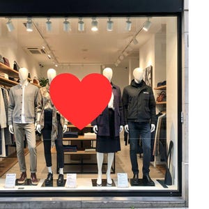 Könnte beinhalten: Schaufenster mit Schaufensterpuppen, die verschiedene Outfits tragen. Die Schaufensterpuppen präsentieren eine Reihe von Kleidungsstücken, darunter Jacken, Hemden, Hosen und Röcke. Das Innere des Geschäfts ist sichtbar, mit Regalen, die zusätzliche Waren ausstellen.