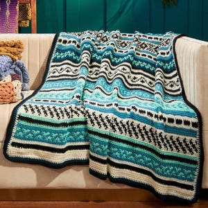 May include: A rectangular crochet blanket featuring horizontal bands of geometric patterns in shades of teal, turquoise, white, and black. The textile displays intricate stitch work with repeating motifs, finished with a solid black border edge.