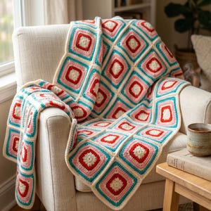 May include: A handmade crochet blanket in a repeating square pattern of red, pink, turquoise, and cream, draped over a cream armchair. The blanket's design is intricate, with each square outlined in a contrasting colour, creating a visually appealing textile.