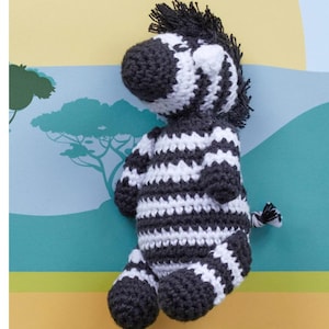 May include: A handmade crochet zebra toy in black and white stripes. The stuffed animal has a dark gray mane and tail, and is posed on a colorful background with a savanna theme. The zebra is a cute and cuddly toy.