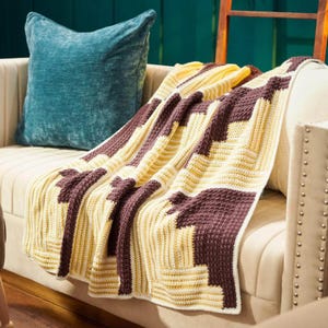 May include: A crochet blanket featuring a geometric pattern of dark brown and cream-colored yarn. The design consists of alternating rectangular blocks arranged in a stepped, interlocking layout with a textured, ribbed stitch throughout.