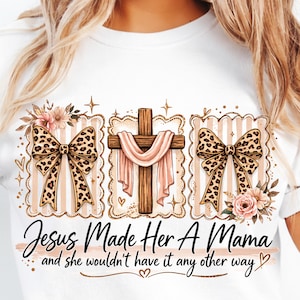 May include: White t-shirt with a design including a wooden cross draped with pink fabric, leopard print bows, and floral details. The text reads "Jesus Made Her A Mama" and "and she wouldn't have it any other way."
