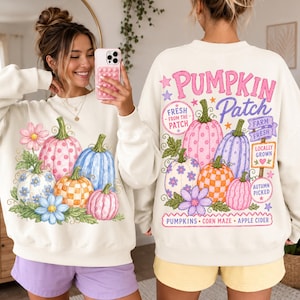 Op de afbeelding: Een crèmekleurig sweatshirt met ronde hals en een kleurrijke afbeelding van pompoenen en bloemen. De voorkant toont een groep pompoenen met patronen, terwijl de achterkant de tekst PUMPKIN PATCH bevat met extra boerderij-thema labels.