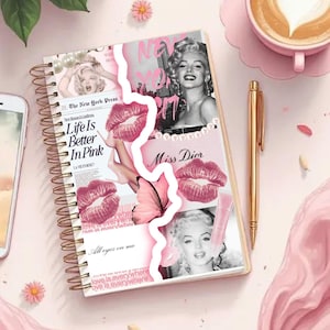 May include: A spiral-bound notebook with a collage design featuring Marilyn Monroe, pink lipstick, and the text "Life Is Better In Pink." A gold pen and a cup of coffee are also visible.
