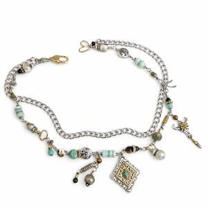 May include: A silver chain belt with various charms, including beads, a diamond-shaped pendant, and a bull skull. The belt features a gold clasp and a heart-shaped connector.