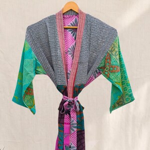 May include: A long-sleeved robe featuring a patchwork design with various patterns and colors including black, white, teal, pink, and purple. The garment has a wide collar, an open front, and a matching fabric tie belt at the waist.