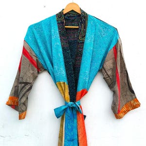 May include: A long-sleeved kimono robe featuring a patchwork design with vibrant panels of turquoise, orange, yellow, and dark patterned fabric. The garment includes a matching tie belt at the waist and a dark, intricate paisley-patterned collar.