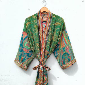 May include: A long-sleeved kimono robe featuring a vibrant green base with a multi-colored paisley pattern. The garment includes a matching tie belt at the waist and a contrasting decorative border along the front opening and sleeve cuffs.