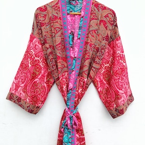 May include: A long-sleeved kimono robe featuring a vibrant patchwork of red, pink, and teal paisley patterns. The garment includes a matching fabric tie belt at the waist and a contrasting teal and pink border along the front opening and collar.