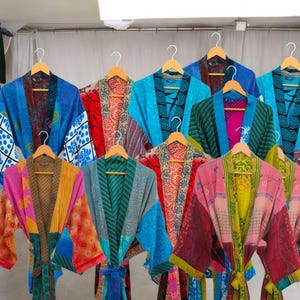 May include: A collection of colorful, patterned robes hanging on wooden hangers. The robes feature a variety of designs, including floral, geometric, and abstract patterns. The color palette includes blues, pinks, greens, and reds. The robes are made of a lightweight fabric.
