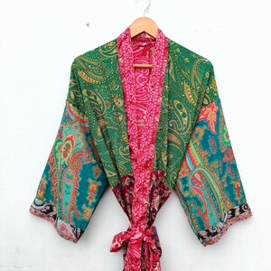 May include: A long-sleeved kimono robe featuring a vibrant patchwork design with various paisley patterns. The garment displays a color palette of emerald green, bright pink, and teal, with a matching fabric tie belt at the waist.