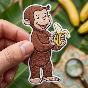 May include: Embroidered patch featuring a smiling brown monkey holding a peeled yellow banana. The monkey has a white outline and is set against a background of green leaves and bananas. A fun, colorful patch.