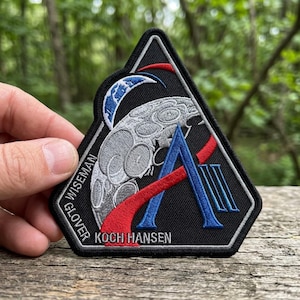 May include: A white ceramic mug with a black handle and the text "But First, Coffee" in a bold, black font. The mug is set against a neutral background, highlighting its simple design.