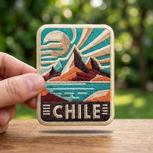 May include: Embroidered patch featuring a mountain landscape with a teal sky and sunburst design. The patch includes a lake, mountains, and the word "CHILE" in a bold font. The patch is rectangular with a stitched border.