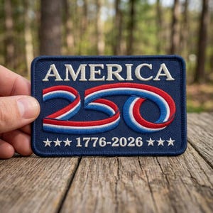 May include: A navy blue patch with the word "AMERICA" in white block letters. The number "250" is displayed in red, white, and blue. The text "1776-2026" and three stars are at the bottom. The patch is rectangular.