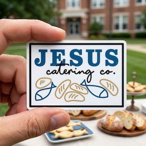 May include: A rectangular sticker with the text "JESUS catering co." in blue and black. The sticker features illustrations of bread loaves and fish in blue and tan. The sticker is held in a person's hand.