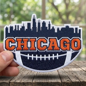 May include: Embroidered patch featuring the city skyline of Chicago above the word "CHICAGO" in orange, set against a navy blue background. The design incorporates a football shape with white stitching, perfect for sports fans.
