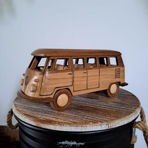 Peut inclure: Un jouet en bois représentant un van classique. Le van est fabriqué en bois clair avec des détails plus foncés, notamment les fenêtres et les roues. Il est posé sur une surface en bois rustique. Le design du van est détaillé.