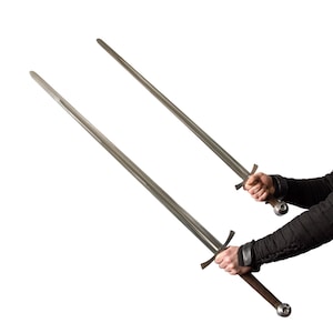 May include: Two long, silver swords with cross-shaped hilts and brown handles are held against a white background. The swords are angled, with the blades pointing upwards. The handles have a rounded pommel.