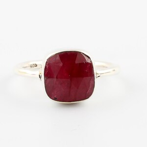 Pu&ograve; includere: Un anello d'argento con una grande pietra preziosa di rubino a taglio quadrato. Il rubino &egrave; di colore rosso intenso ed &egrave; incastonato in una fascia semplice ed elegante. L'anello &egrave; esposto su sfondo bianco.
