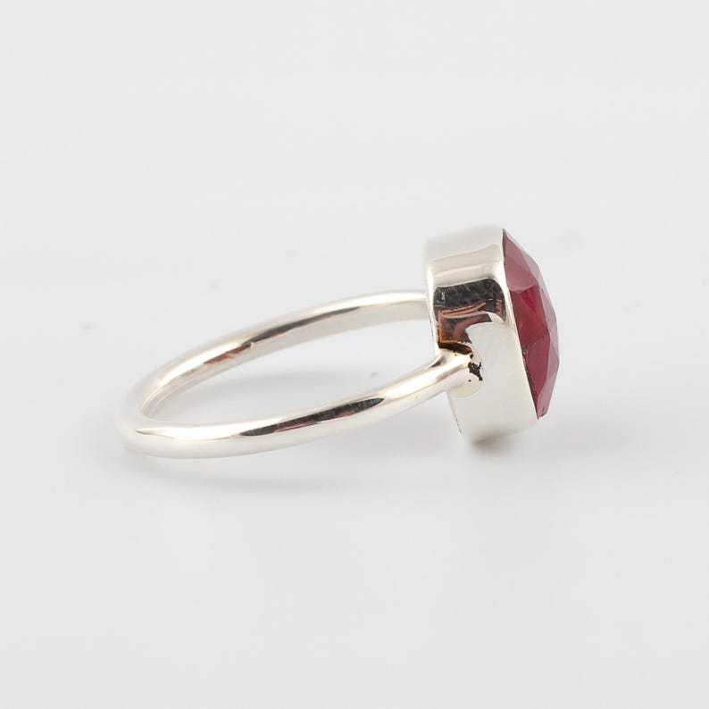 Pu&ograve; includere: Un anello d'argento con una grande pietra preziosa rossa sfaccettata. L'anello ha una fascia semplice e lucida e un'incastonatura quadrata che tiene la vibrante pietra rossa. Le sfaccettature della pietra preziosa catturano la luce, creando un effetto scintillante.