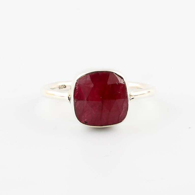 Pu&ograve; includere: Un anello d'argento con una grande pietra preziosa di rubino a taglio quadrato. Il rubino &egrave; di colore rosso intenso ed &egrave; incastonato in una fascia semplice ed elegante. L'anello &egrave; esposto su sfondo bianco.