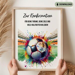 以下が含まれることがあります： ユーロ紙幣の模様が入ったサッカーボールと、カラフルなペンキの飛沫が描かれたスタジアム背景の額入りプリント。テキストは「Zur Konfirmation, FÜR DEINE TRÄUME, DEINE ZIELE UND VIELE VOLLTREFFER IM LEBEN!」と記載されています。