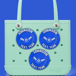 May include: A light green tote bag with three blue circular charms. Each charm has the name "JOHNSON", the words "TEXT, YEAR", and a white emblem. The bag has a blue background and white handles.