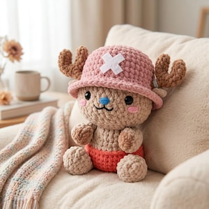 May include: A crocheted plush toy of a cartoon character, with a pink hat and white cross, brown antlers, and a red diaper. The toy is beige with a blue nose and pink cheeks, sitting on a cream cushion.