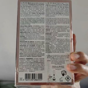 May include: A box of Lanc&ocirc;me La Vie Est Belle perfume. The packaging is a light pink with text in multiple languages. The bottom of the box has a barcode and the text "MADE IN FRANCE".